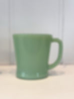 Front view of a vintage Fire-King jadeite D-handle mug with its iconic flared silhouette and luminous green glass.