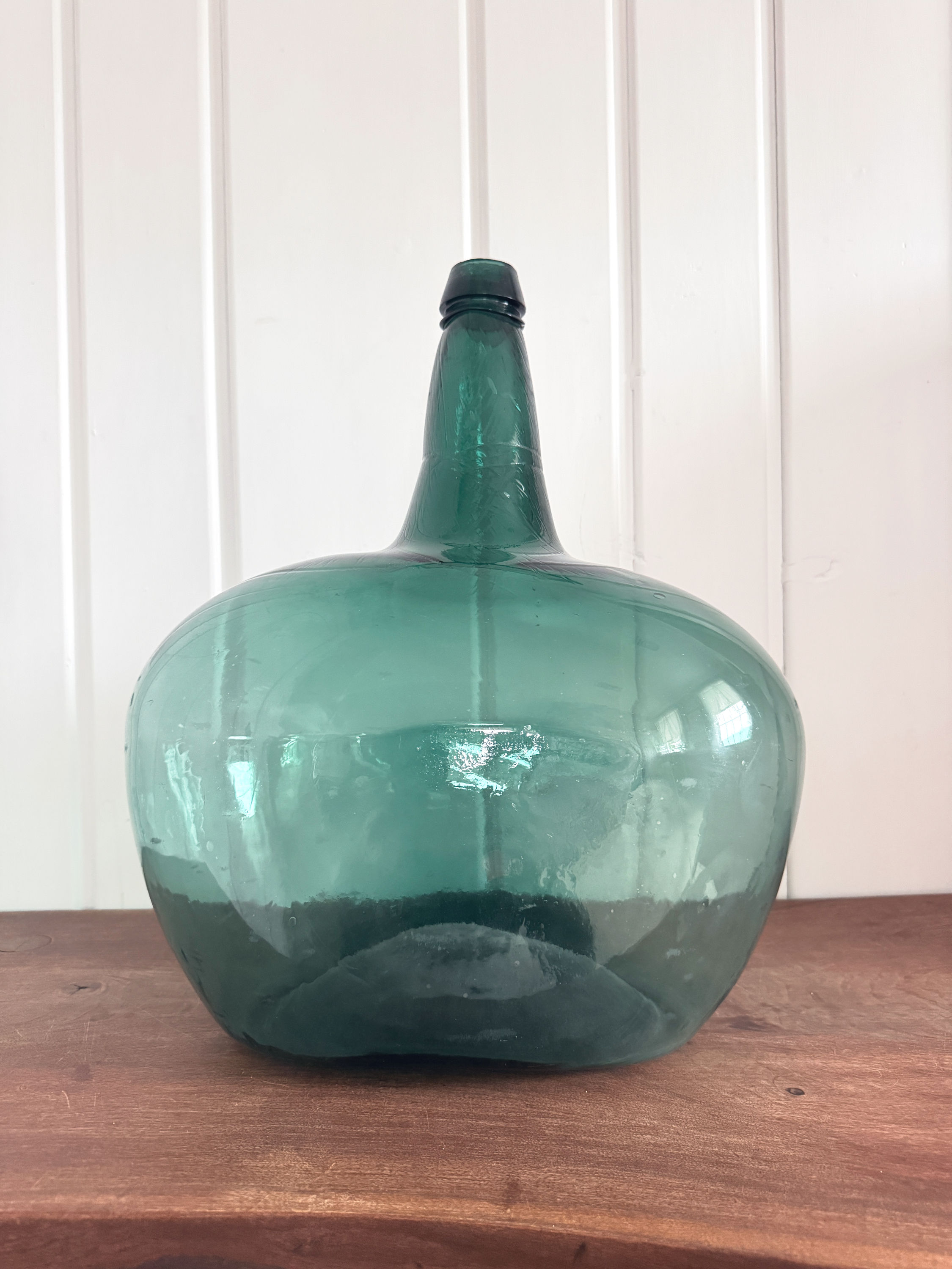 Rear view of a large antique European blue-green glass demijohn with a rounded onion-shaped silhouette.