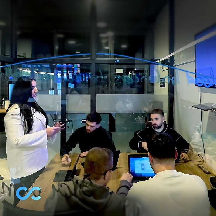 A professional team in a modern office environment. A female team leader stands confidently while presenting to her team, who are seated at a table with laptops, engaged in discussion. The scene reflects collaboration, technology, and a focus on IT solutions, with a glass-walled meeting room and visible digital displays in the background
