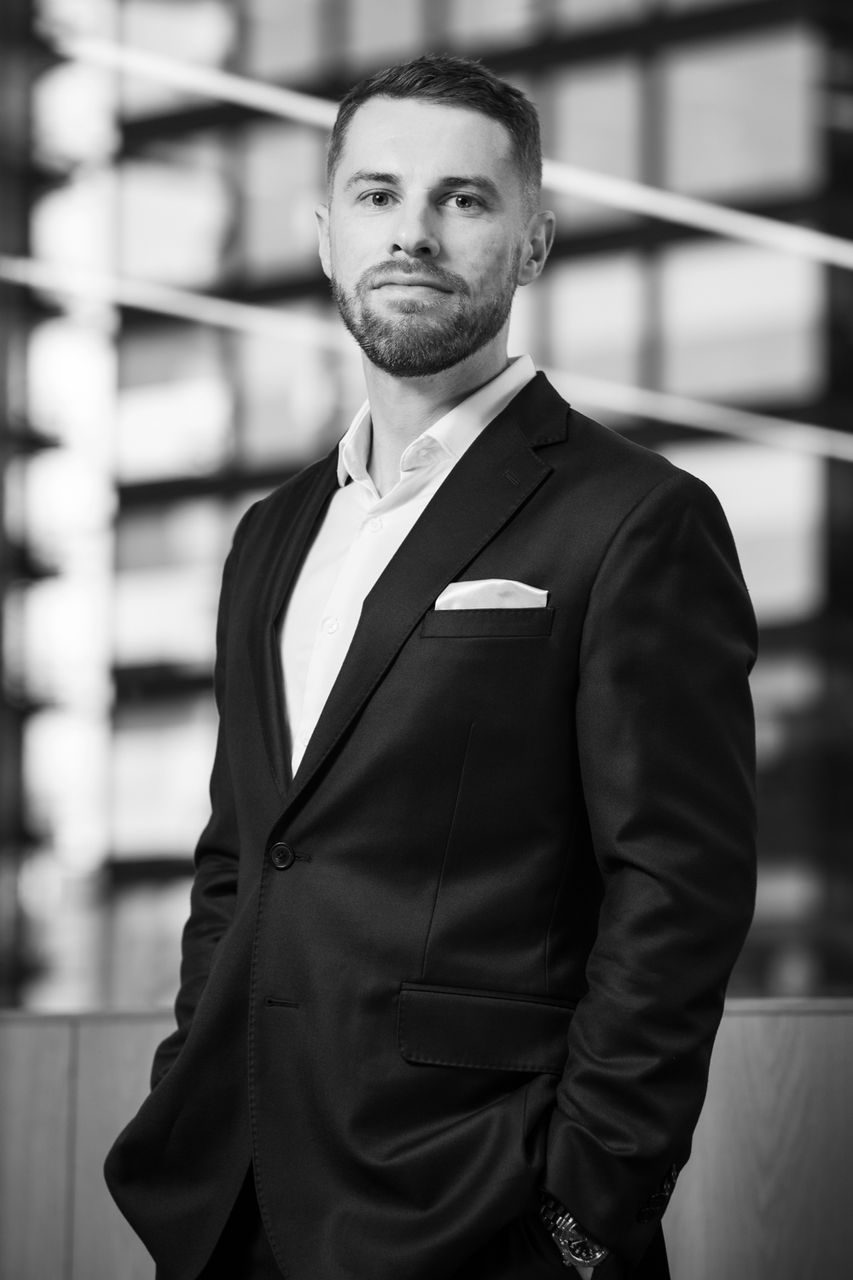 a man wearing a casual suit is staring into the camera. the background is of an office building. taken on location by Future Proof