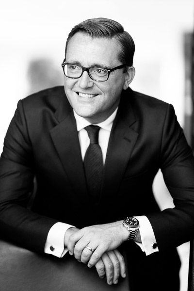 a black and white image of a man in a suit wearing glasses. He is leaning towards the camera and looking to the left. It is a professional image of a professional man taken at an office by Future Proof Photography