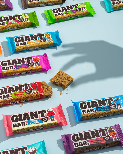 A creative food photography shoot of flapjacks lying on a pale blue background. One piece of flapjack has been placed to look eaten and there is a shadow of hand giving the appearance of grabbing it