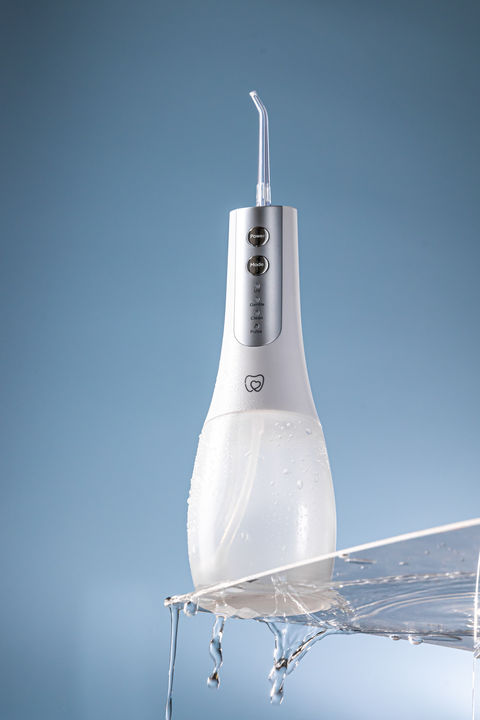 water splashing on a water flosser which has been placed on a white shelf. there is water falling off the shelf