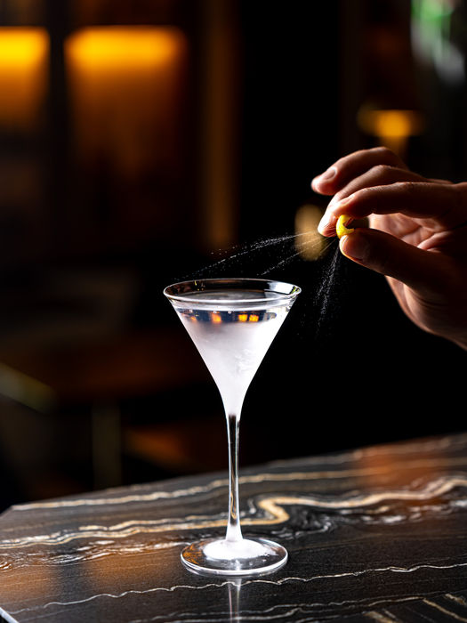 Hand model squeezes fruit into a martini glass in a dark pub. Modern, edgy, stylish drink photography