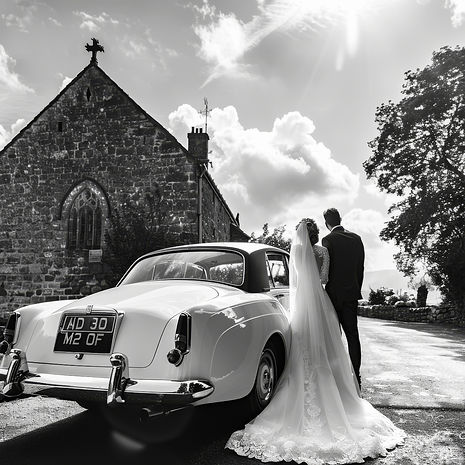 A bride and groom stand beside a classic white car outside a stone chapel, an essential wedding photo for timeless elegance.