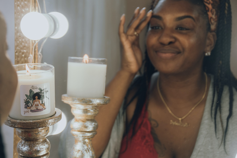 Mulher negra olhando seu reflexo no espelho, enquanto toca seu rosto e sorriem seu rosto enquanto sorri