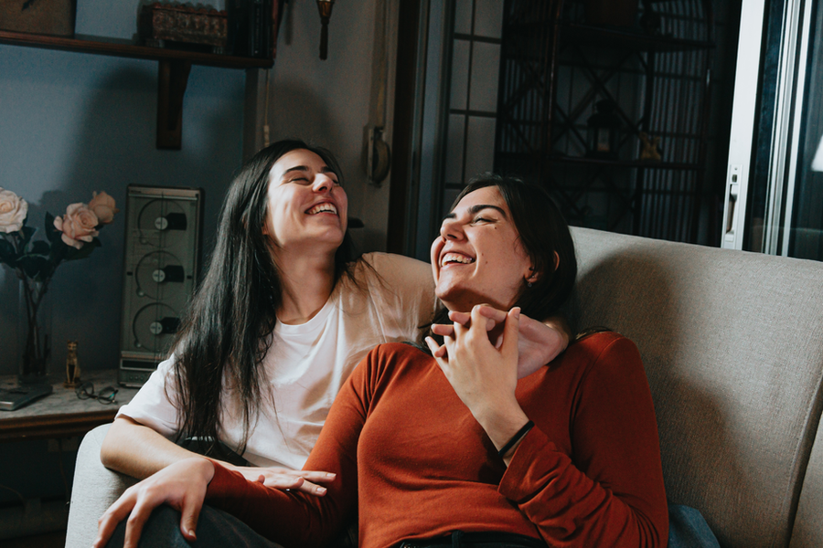 casal de mulheres abraçadas em um sofá, de mãos dadas e sorrindo
