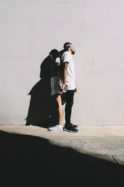 Casal de costas um para o outro de mãos dadas e com bastante sombras
