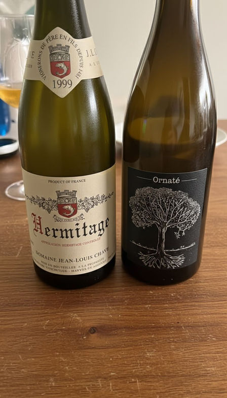 Deux bouteilles de vin photographiées de près sur une table, dont un Hermitage blanc de Jeal-Louis Chave 1999 et une cuvée Ornate, étiquettes visibles.