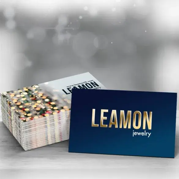 Two stacks of raised foil business cards. One stack is white, and the other is blue, both displaying the word 'LEAMON'.