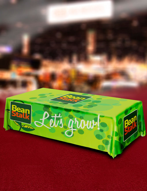 Rectangular table draped in a green full‑color table cover featuring Let’s Grow logo and leaf graphics