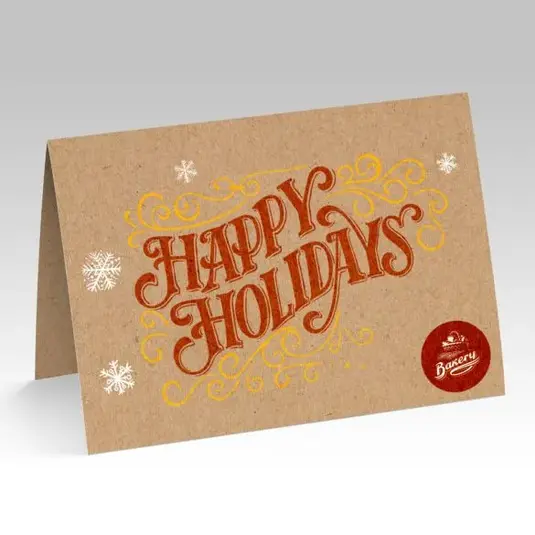 Folded kraft holiday card with “Happy Holidays” in orange script and small brand stamp