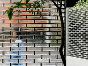 這是一間在臨街上的庭院圍牆設計，不再是傳統紅磚，而是選擇砌上透明的實心玻璃磚，粼粼波光的陽光灑落於中庭、照亮了空間，庭院的綠色植栽更顯綠意盎然、隨之蕩漾。這樣生氣勃勃地景象也和戶外產生了連動，從外面看進來似清悠自然地雅築；從裡面看出去似人來人往的街景，無形之中成了一幅會動的畫作。