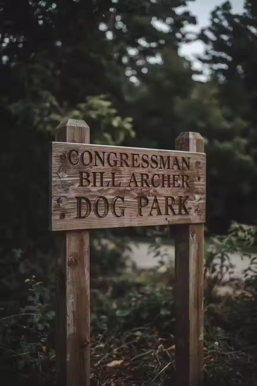 A Photo of the sign to "Congressman Bill Archer Dog Park" with tree's in the background almost covering it.