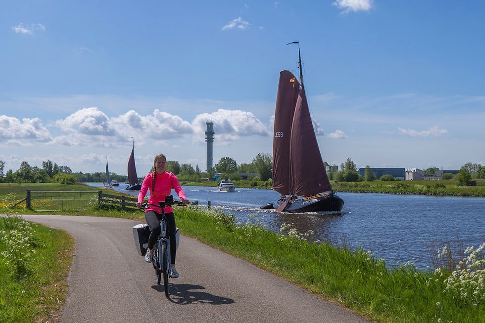 Vrouw fiets langs een kanaal in Friesland waar een skûtsje vaart