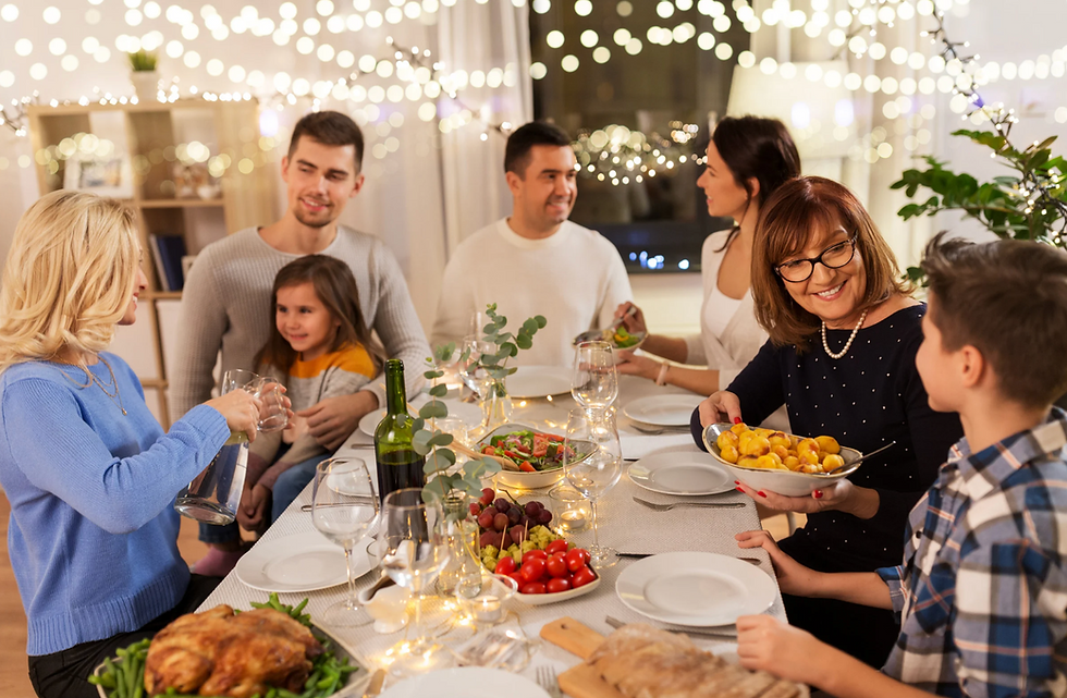 Family gathers at a warmly lit dinner table, sharing food and smiles. Festive decor with string lights enhances the cozy atmosphere.