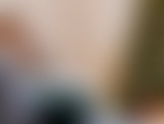 Woman on a couch with a blanket, looking pensive. Christmas tree in the background with lights. Red cup and oranges on table. Cozy setting.