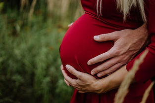 pregnant woman wearing a red dress, her hand and her partners hand lie on the big baby belly