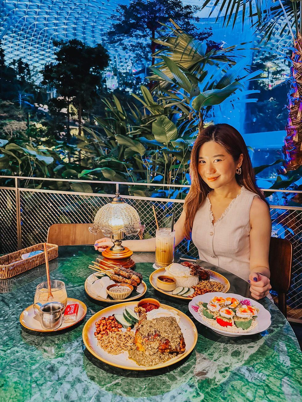 Juliana and Bobby at Wild Coco's flagship store at Jewel Changi Airport, featuring the Jewel exclusive menu including the Coco J coconut shake, Kueh Pai Tee served on vintage plates, Ayam Bakar Nasi Lemak, and the stunning tropical Southeast Asian interior with views of the iconic Rain Vortex.