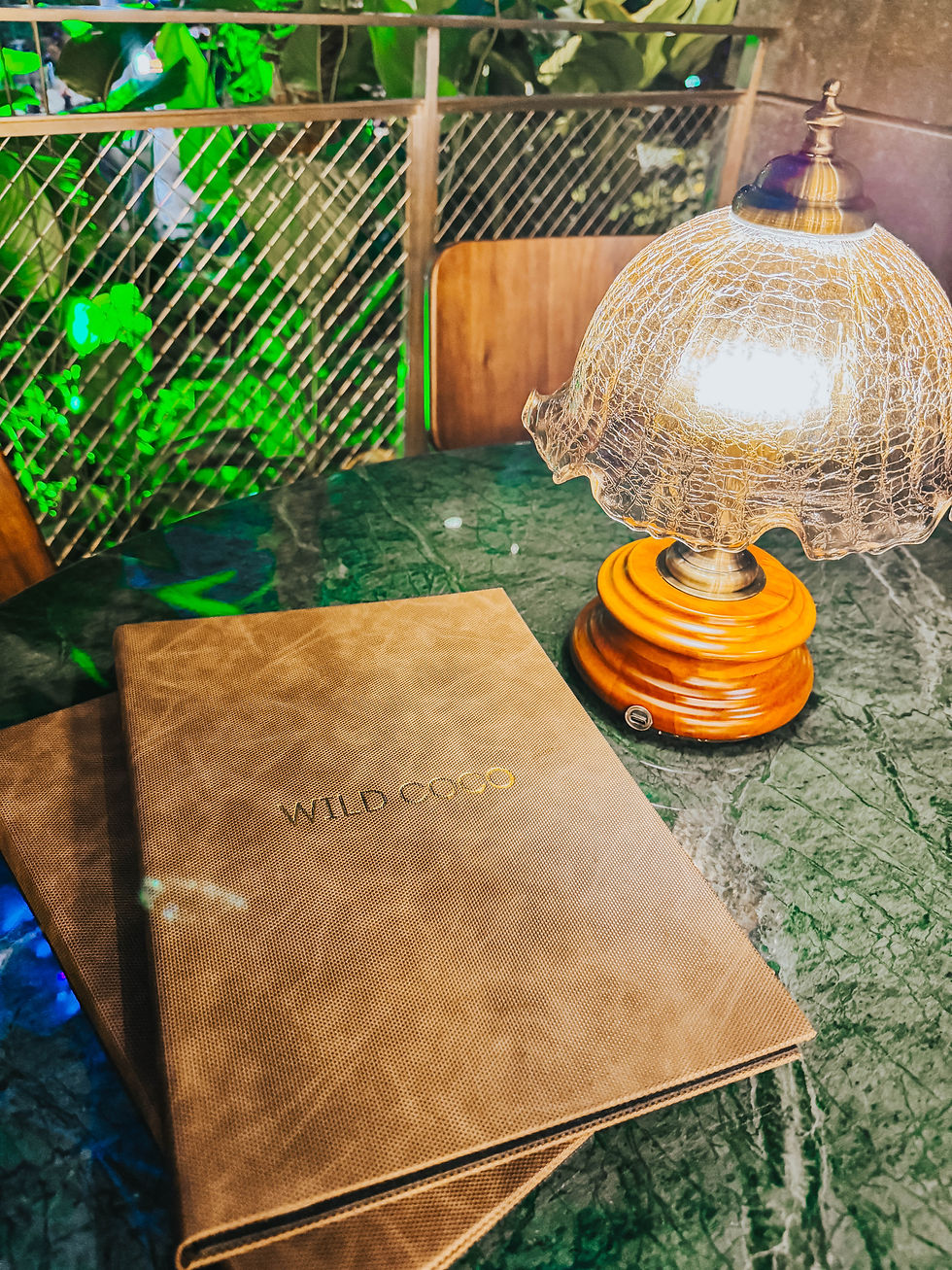 Juliana and Bobby at Wild Coco's flagship store at Jewel Changi Airport, featuring the Jewel exclusive menu including the Coco J coconut shake, Kueh Pai Tee served on vintage plates, Ayam Bakar Nasi Lemak, and the stunning tropical Southeast Asian interior with views of the iconic Rain Vortex.