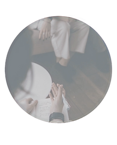 Person writing on paper, hands in front of a person visible in background.