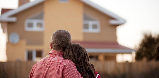 Couple embracing and looking at their home, representing protection and home insurance.