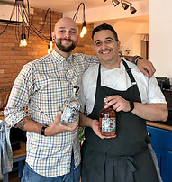 Two of the team at St. Martha Greek Restaurant, holding a bottle of Nantwich Gin and a bottle of Sweet Briar gin.