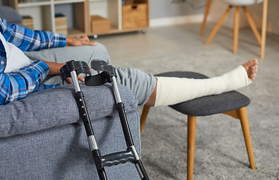 Person sitting on couch with injured foot propped up and crutches leaning against couch