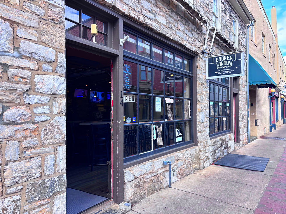 Stone-front Broken Window Brewery storefront with open door and hanging sign on a quiet sidewalk.