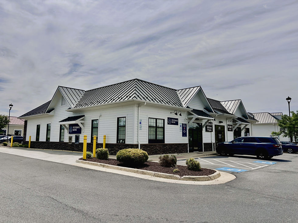 Bank storefront in a white building with black metal roof, parking lot, and blue SUV under cloudy sky.