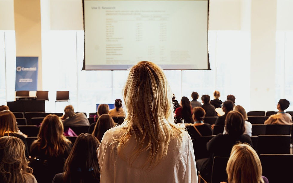Image of person with long blonde haired walking down the aisle of a lecture theatre about to present at a conference.