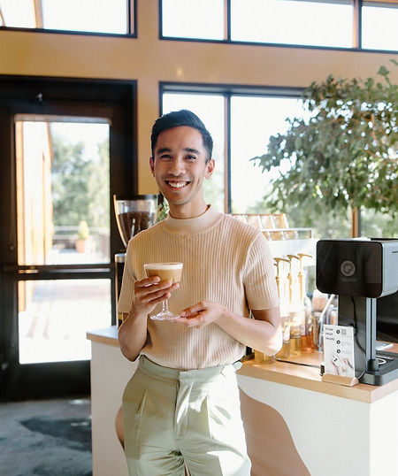 Man stading in front of a coffee cart holding a drink smiling