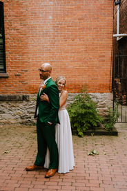Bride hugging groom in front of brick wall.