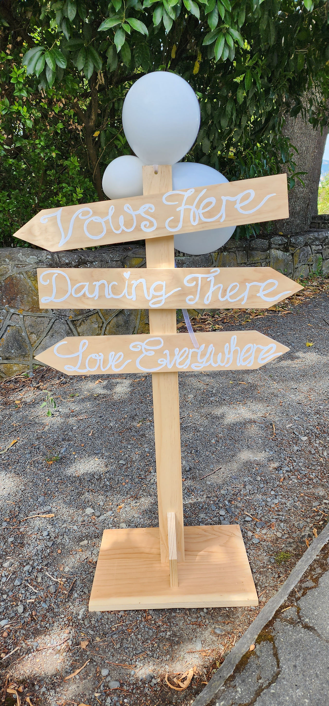 A wooden sign set up at a wedding rehearsal with arrows pointing in different directions, saying vows here, dancing there, love everywhere