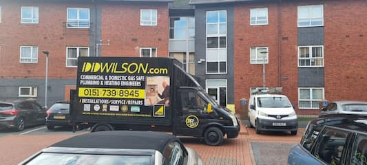 Black van with "DDWILSON.com" ad parked outside red brick apartments. Contact info in bold yellow. Other cars nearby.
