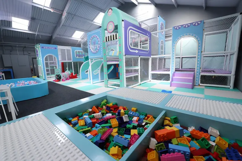 Large pastel colour indoor play area in the foreground lego building blocks and in the background a large play area