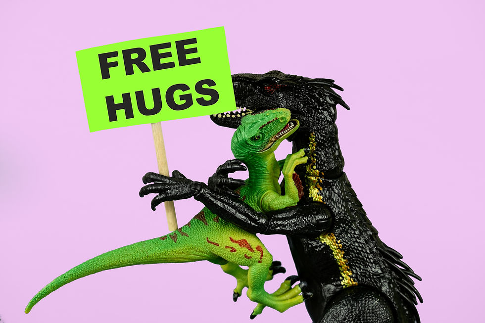Due dinosauri giocattolo si abbracciano su sfondo rosa mentre uno regge un cartello verde con la scritta “FREE HUGS”.