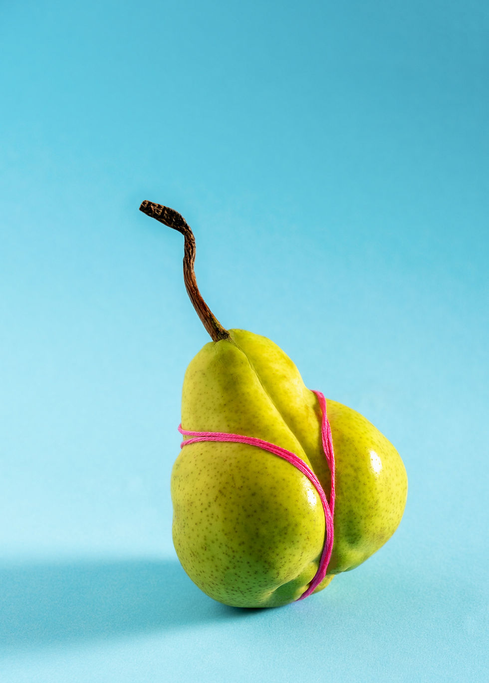 Pera verde su sfondo blu con elastici rosa posizionati come un bikini. Fotografia concettuale minimalista.