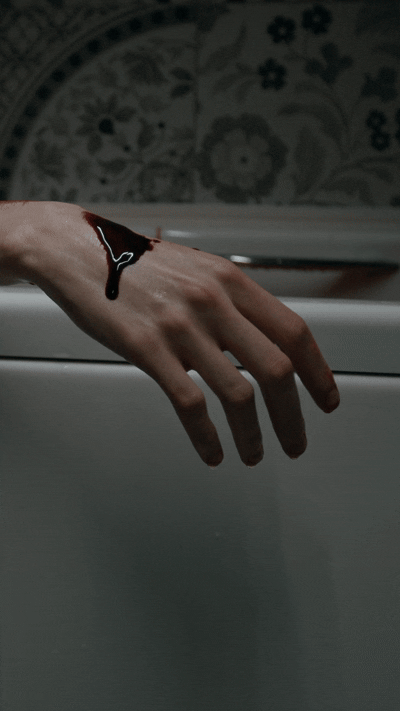 Mano che sporge dal bordo di una vasca bianca con una ferita sanguinante sul polso.