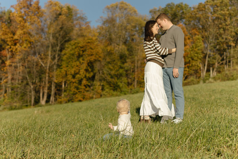 Mom and dad cuddle with a little in the grass