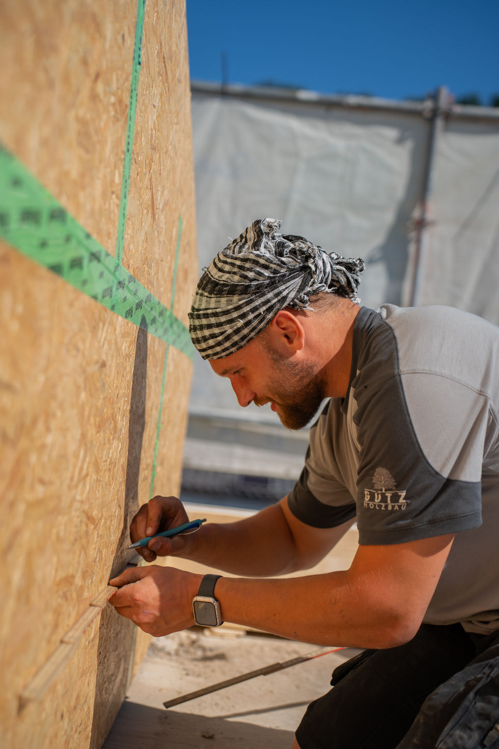 Mann misst mit Zollstock eine Holzwand aus und markiert Maße.