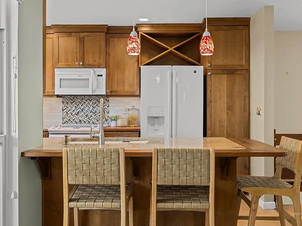 Modern kitchen with wooden cabinets, white appliances, and a chevron backsplash. Three woven chairs at the island, with red pendant lights. Boise Idaho