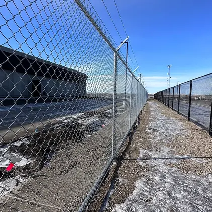 Chain link fence along a sidewalk, clear blue sky background, sunny day view.