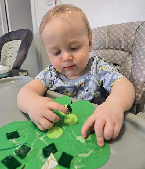 Toddler in high chair decorating a green shamrock craft project.