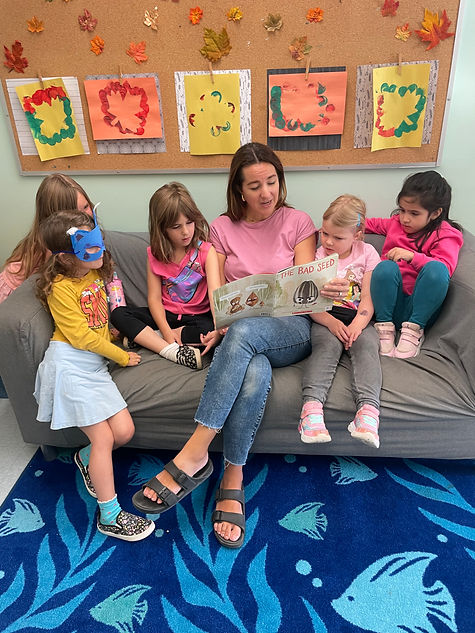 Teacher reads to children, art decorates wall, happy expressions, joyful reading time.
