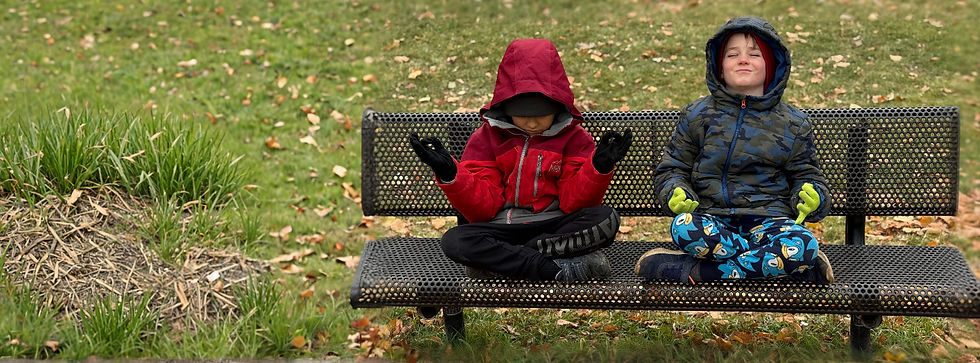 Two children in hooded jackets meditating on a park bench.