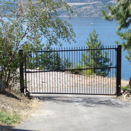 Black metal gate entrance with lake view and trees in background.