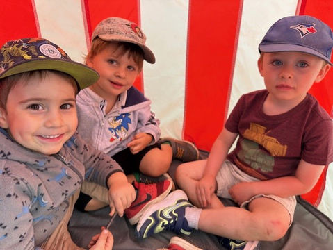 Three young boys in hats sitting inside a red and white tent