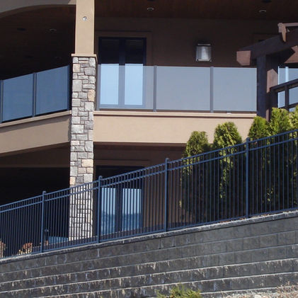 Luxury home exterior with glass balconies, trees, and stone retaining wall.