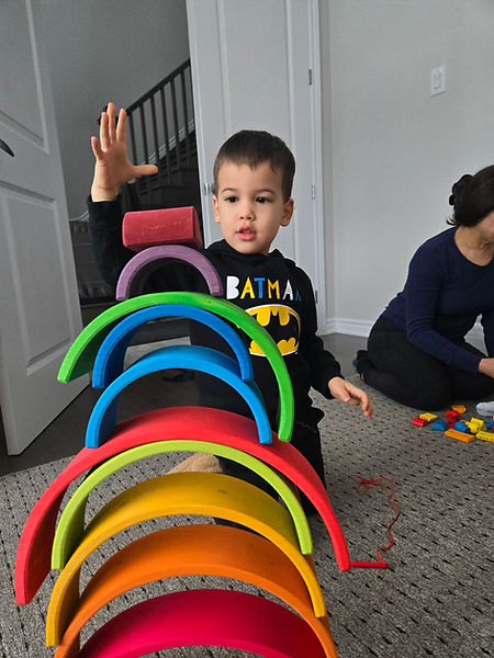 Child in BATMAN shirt stacks colorful rainbow arches indoors